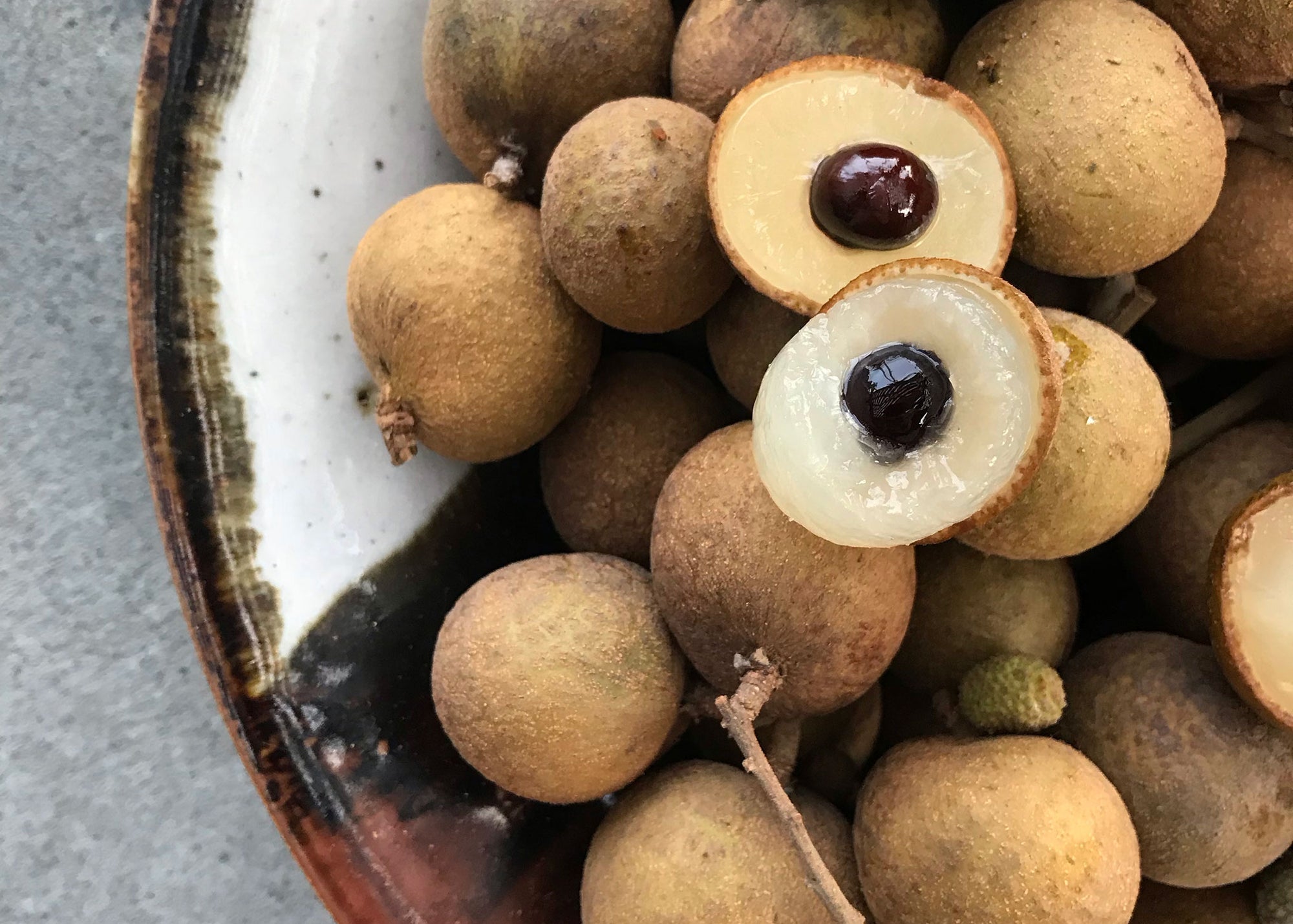 Fresh longan fruit from Hawaii. Image of longan fruit in a bowl with a few fruits open with the seeds and flesh showing.