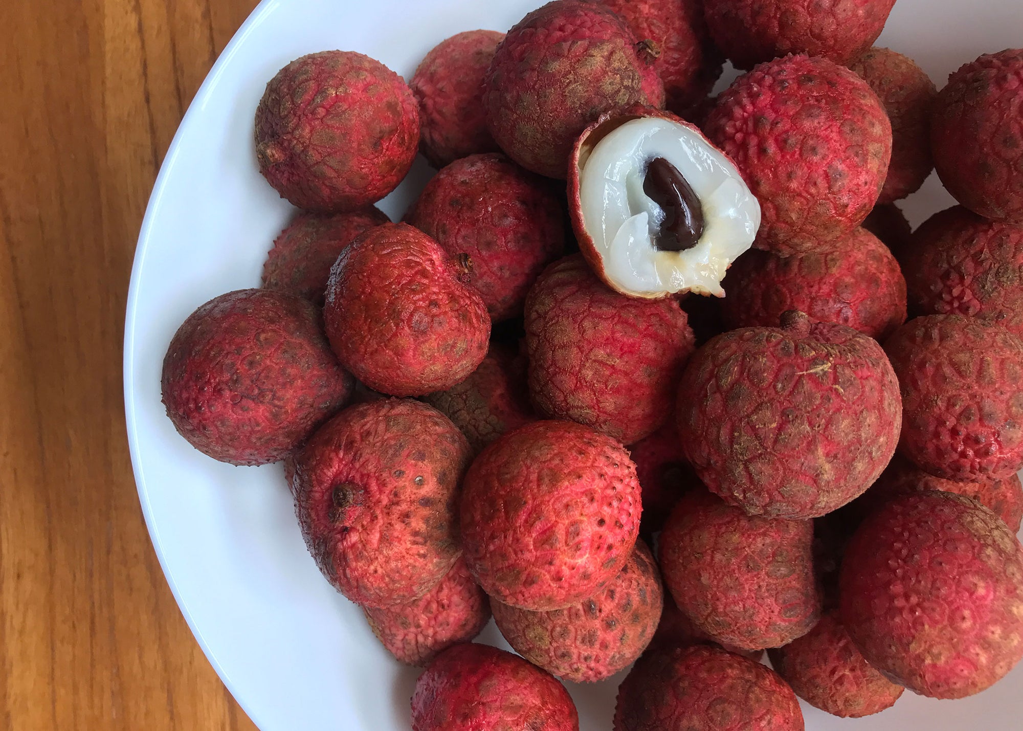 Fresh kaimana lychee fruit from Hawaii. Image of lychee fruit in bowl with one fruit peeled open to show fruit flesh and seed.